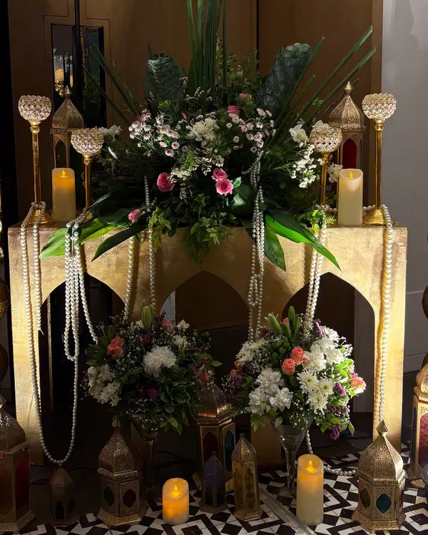 An opulent decor corner for a 10th-anniversary party. This setup features Moroccan-style lanterns, pearl strings, and floral arrangements on a carved table, creating a rich and romantic atmosphere.