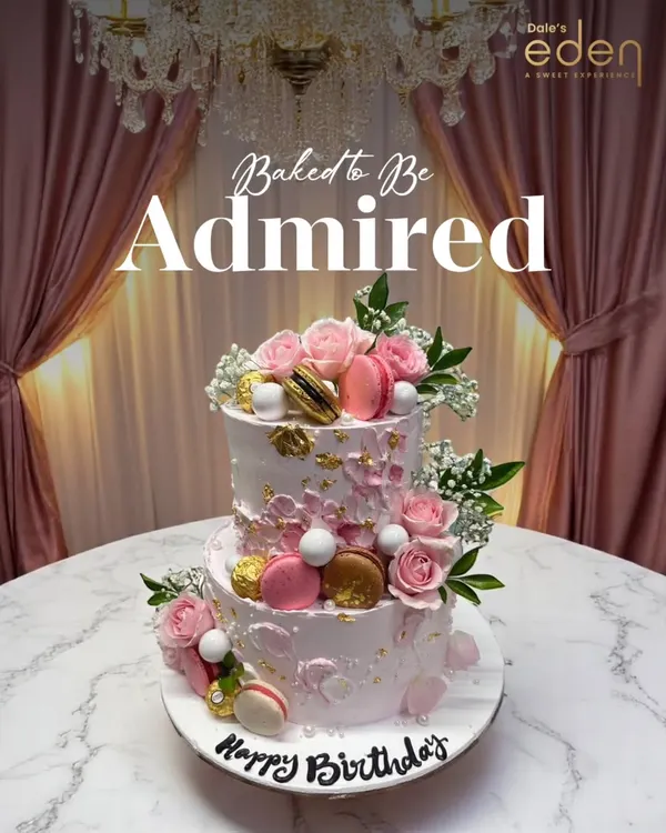 Baked to be admired. This exquisite two-tier birthday cake features delicate pink roses, macarons, and gold leaf accents, creating a look of pure elegance and luxury.