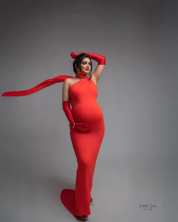 Owning the moment in a striking red halter gown. This look is all about celebrating your confidence and power, with a flowing scarf that adds a touch of dynamic elegance to this fashion-forward maternity portrait.