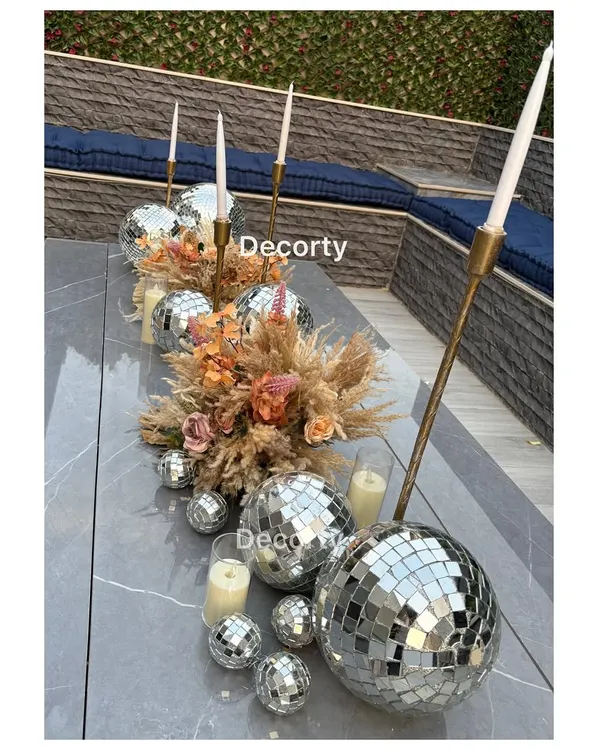 An ultra-chic table centerpiece for a 'Disco Night' adult birthday party. The runner is made of disco balls of various sizes, dried pampas grass, and tall, elegant candle holders.