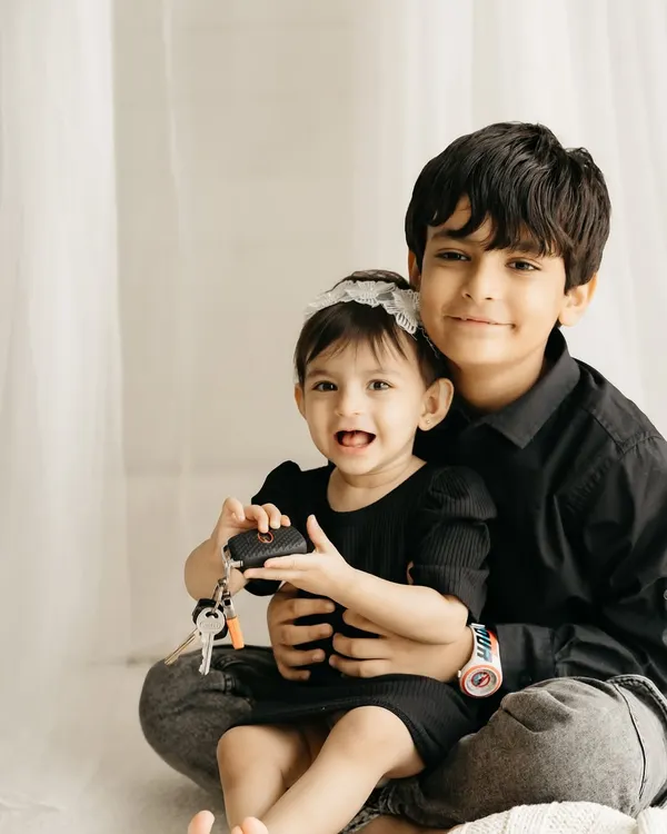 An older brother holds his baby sister, who is happily playing with a set of keys. A real, candid sibling moment.