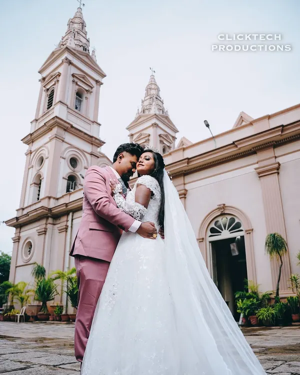 A beautiful wide-angle shot of a Christian bride and groom embracing in front of the church, with the bride's long veil adding a touch of elegance to the portrait.