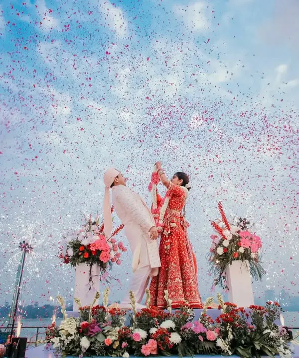 A sundowner varmala by the lake is pure magic. This wide shot captures the stunning sky, the flower shower, and the couple's joy, creating a breathtaking image.