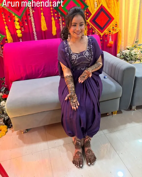 A full view of a happy bride with her complete bridal mehendi. The intricate designs on her hands and feet create a stunning, cohesive look.
