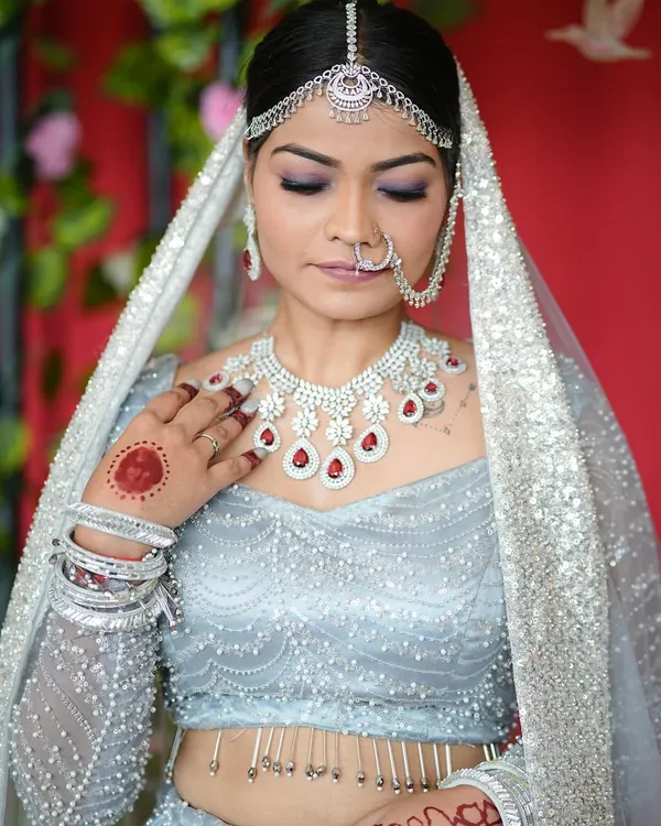 A close-up of a bridal look where the nails are a key accessory. The classic red gel polish on these custom extensions was chosen to perfectly match the ruby details in her necklace and her light blue lehenga.