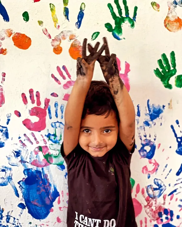 This is what pure, creative joy looks like! We believe in getting a little messy to make something amazing. This happy creator is showing off her paint-covered hands in front of our studio's handprint wall, a testament to all the fun we have.