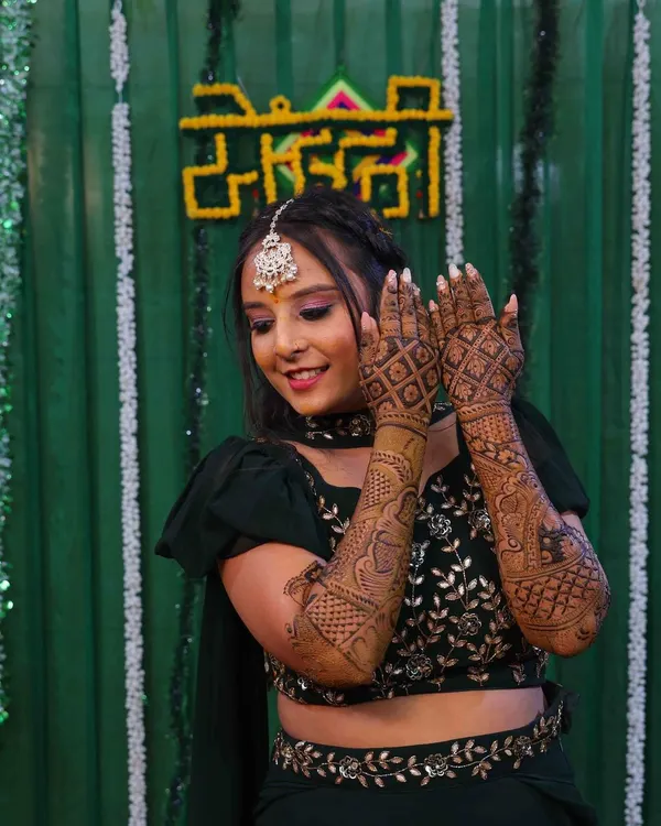A happy bride showing off her full-arm mehndi. The design features a heavy jaal pattern on the back of the hands, perfect for wedding photos.
