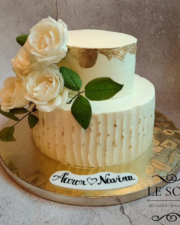 This elegant two-tier cake was for a beautiful wedding celebration. I used a combination of textured buttercream on the bottom tier and a smooth finish with a gold leaf accent on top, all brought together with fresh white roses.