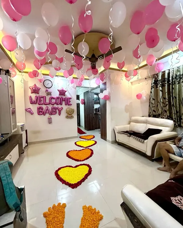 A heartwarming welcome home decoration for a baby girl. The setup fills the living room with pink and white ceiling balloons and features a beautiful pathway of marigold flower hearts leading into the home.