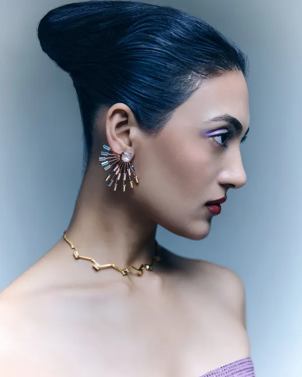 A profile shot from a jewelry editorial, providing a clear view of these stunning fan-shaped earrings and a delicate gold necklace. The model's elegant updo and clean makeup ensure the jewelry remains the focal point.