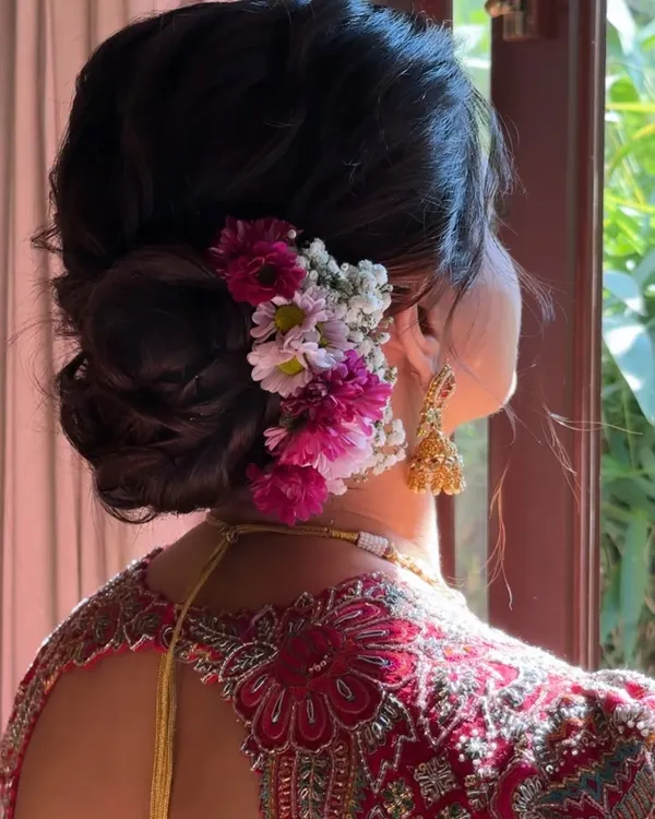 A beautiful detail shot of a classic bridal bun. This hairstyle features a voluminous, textured bun adorned with fresh baby's breath and colorful flowers, adding a touch of romance to the traditional look.