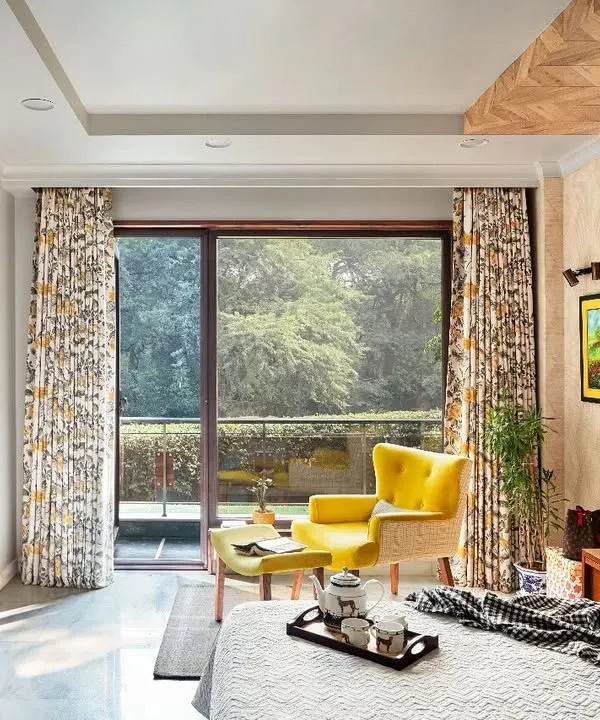 At Ridge View, this bedroom is a personal and expressive space. A herringbone wooden panel on the ceiling adds drama, while a canary yellow accent chair provides a pop of color against the neutral palette, drawing the eye to the lush landscape outside.
