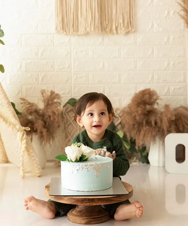 A baby boy sits with his first birthday cake during a boho-themed cake smash session, ready to dig in.