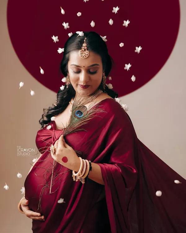This is the art of waiting. In my studio, we used the deep red of a saree, a shower of soft petals, and traditional symbols like the peacock feather to create a portrait that feels like a timeless painting, honoring the universe growing within her.
