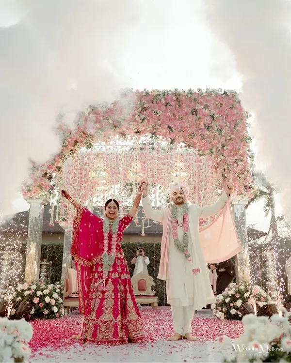 A fairytale moment as the newly married couple stands under a magnificent floral arch, showered with petals and surrounded by sparklers. This is the kind of grand, celebratory shot that defines a wedding day.
