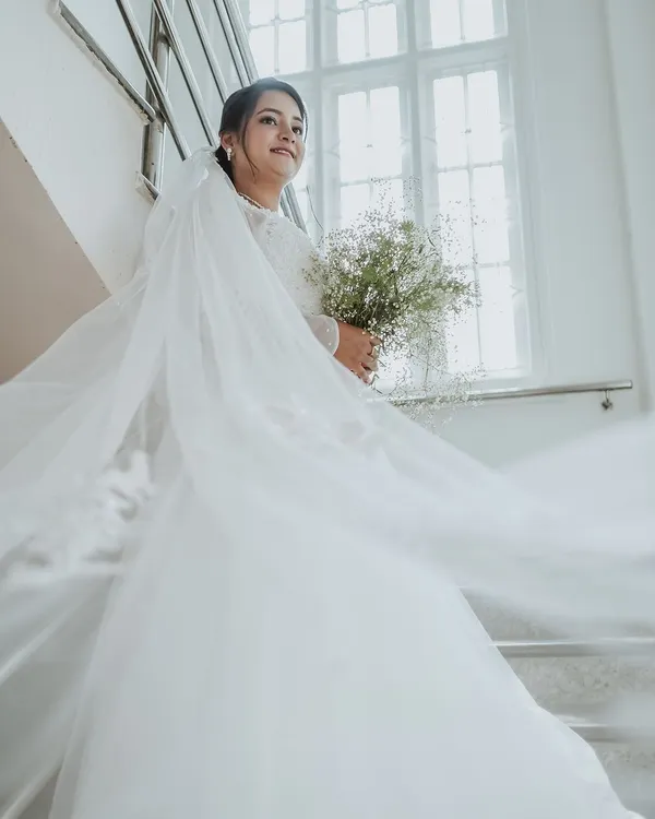 The bride looks ethereal in her flowing white gown and veil, holding a simple bouquet. This shot captures the classic elegance and dreamlike quality of a Christian wedding.