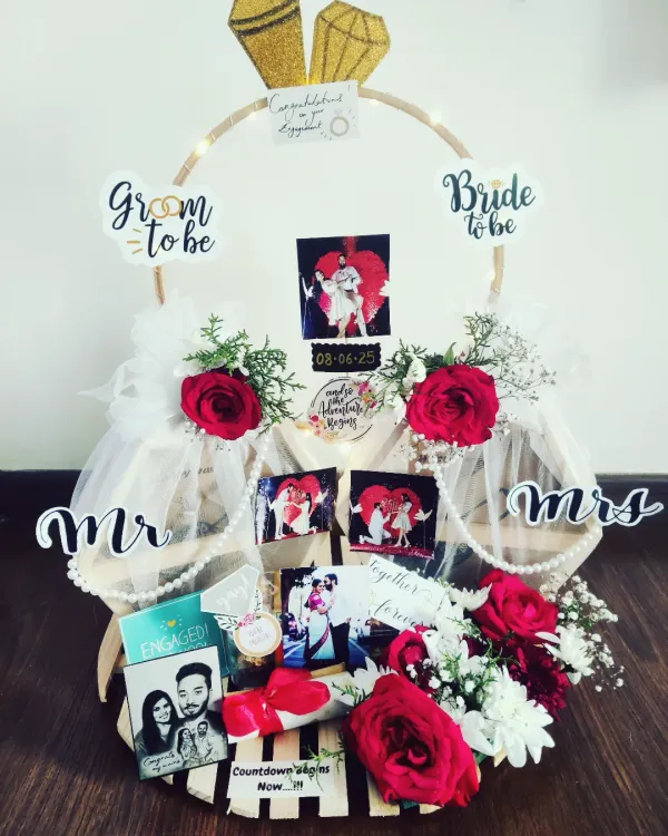 This engagement hamper is designed to celebrate a new beginning. It features a custom ring-shaped platter decorated with fresh flowers, personalized photos of the couple, and fun "Bride to be" and "Groom to be" signs, making it a perfect gift to mark the special occasion.