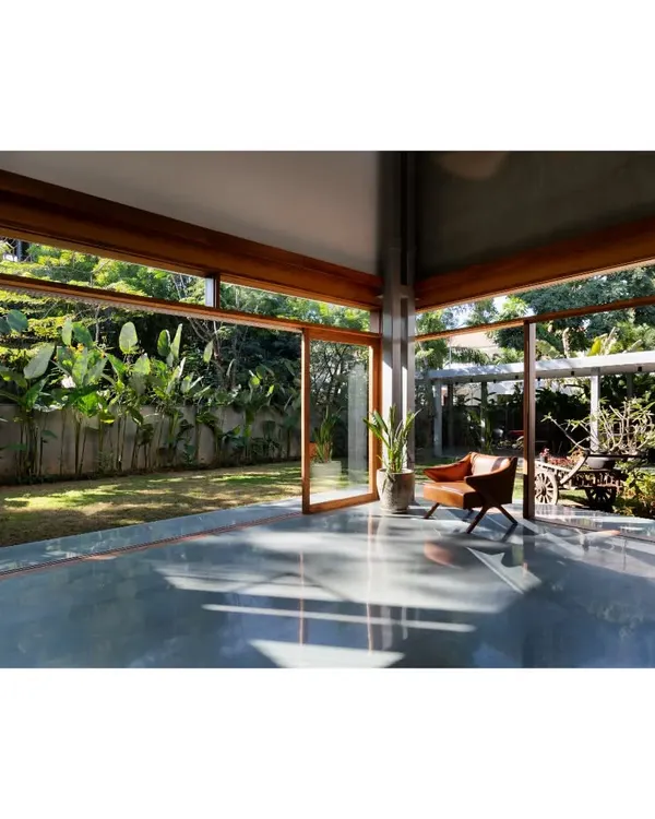 An empty room in the 'House of Canopies' project, where the polished concrete floor reflects the garden outside. The floor-to-ceiling glass doors open completely, transforming the living area into a covered pavilion within the landscape.