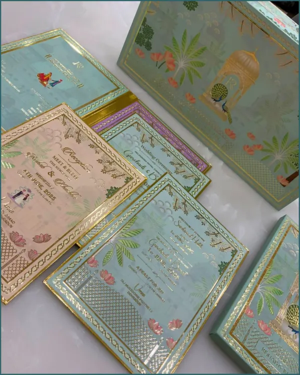 A stunning wedding invitation suite featuring a pastel green box with a peacock motif. The set includes multiple inserts for different events, all coordinated with gold foil detailing for a touch of royalty.