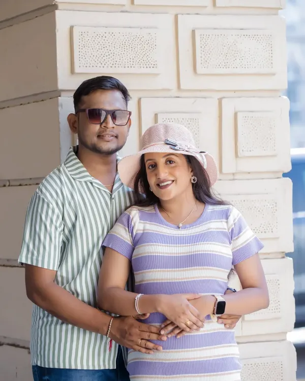 A relaxed and happy couple posing for a maternity portrait against a modern, textured wall. Their casual, coordinated outfits and easy smiles make this a perfect example of a contemporary and informal pregnancy photoshoot.
