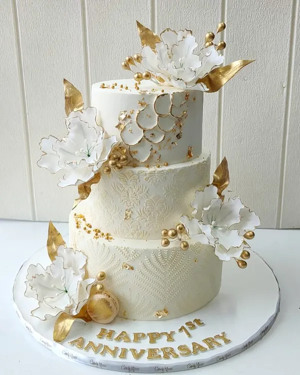 A golden celebration for a golden milestone. This elegant three-tier anniversary cake features intricate textures, delicate white sugar flowers, and luxurious gold accents, designed to reflect timeless beauty and sophistication.