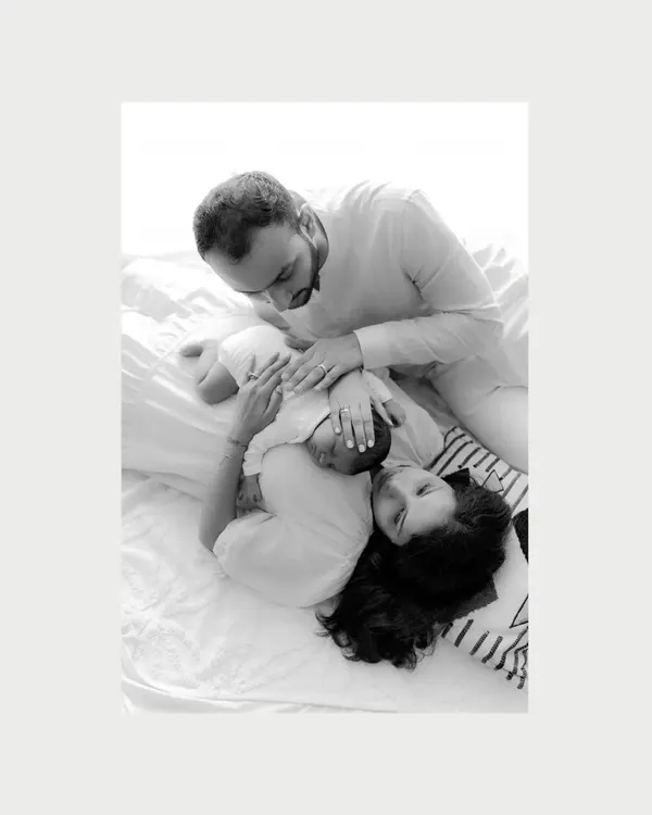 Into the arms from heaven. This black and white photo, taken from above, shows new parents gazing at their baby lying with them, a moment of pure, quiet adoration.