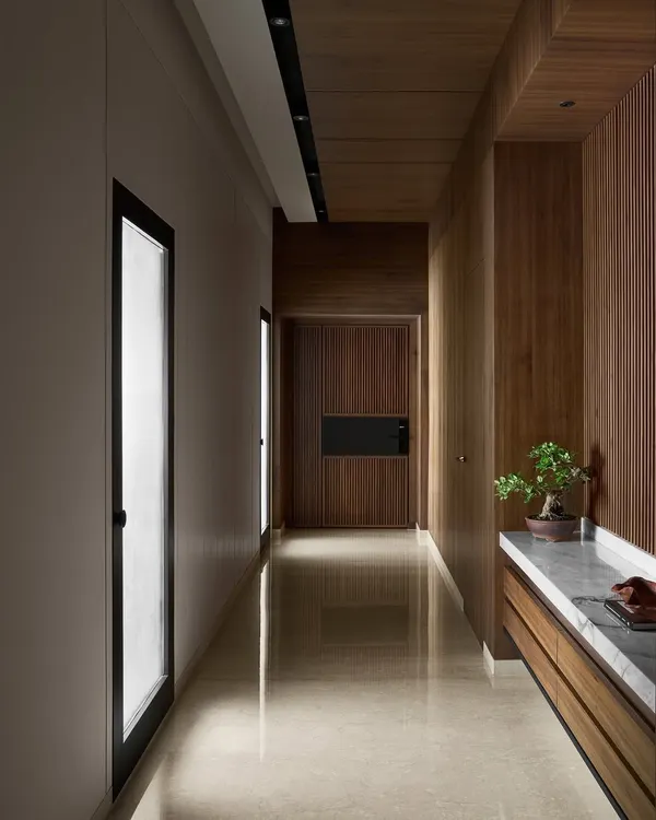 The entrance to Lumen House sets a warm, inviting tone with fluted wood panels and a polished marble floor. The passageway is designed to create a sense of transition, leading the eye towards the bright, open-plan living area.