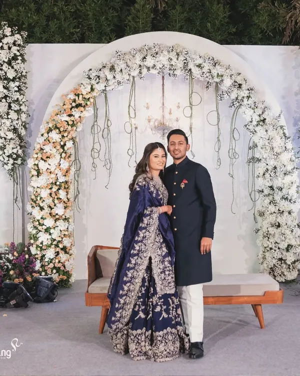 A picture of elegance. The couple stands before a beautiful floral arch of white roses, a classic and timeless backdrop for a reception. My designs focus on creating sophisticated settings for your most important photos.