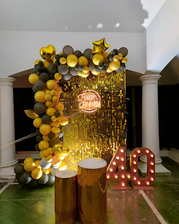 A glamorous 40th birthday celebration with a gold and black theme. This setup features a gold shimmer wall, a balloon half-arch, and large marquee numbers for the age.