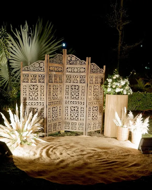 A perfect rustic photo booth for an evening event. We used a carved wooden screen, jute flooring, pampas grass arrangements, and warm spotlights to create this cozy corner.