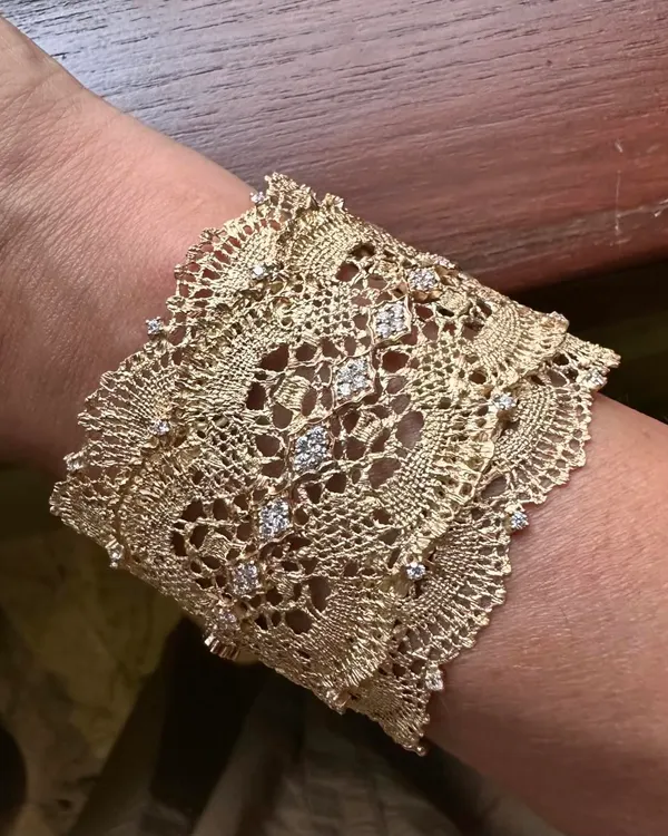 A detailed close-up of my signature lace cuff bracelet. This wide cuff is meticulously hand-woven from 18k yellow gold to resemble fine lace, and is enhanced with scattered natural diamonds.