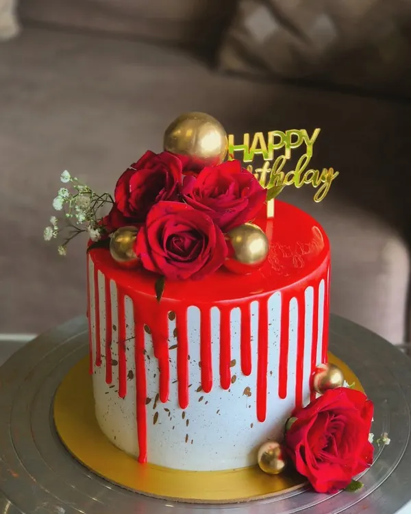 Red and florals can never go wrong. This elegant birthday cake features a bold red drip, fresh red roses, and gold sphere accents for a classic and luxurious look.