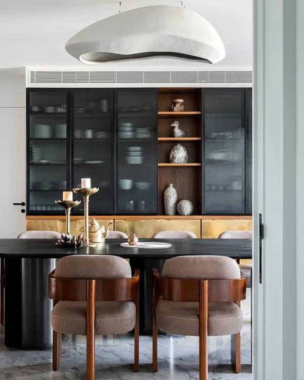 Storage is key in any family home, and these wall cabinets with fluted glass and brass shutters offer both style and function. A bespoke wooden niche showcases curated artifacts, complementing the warm glow of the suspended light.