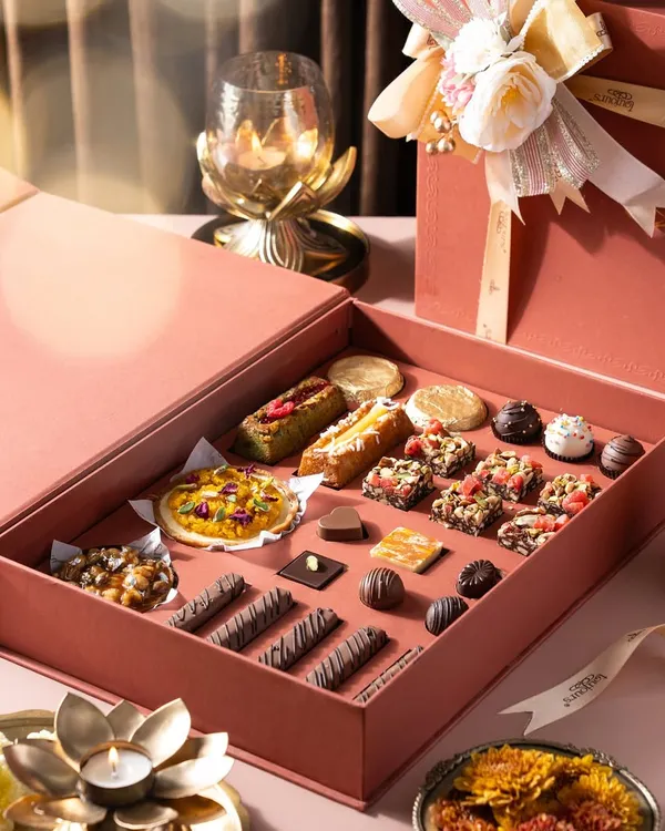 Our premium Diwali gift box, opened to reveal an exquisite assortment of handcrafted sweets. It includes mini tarts, Belgian chocolate pralines, nutty squares, and more, all nestled in a beautiful pink box.