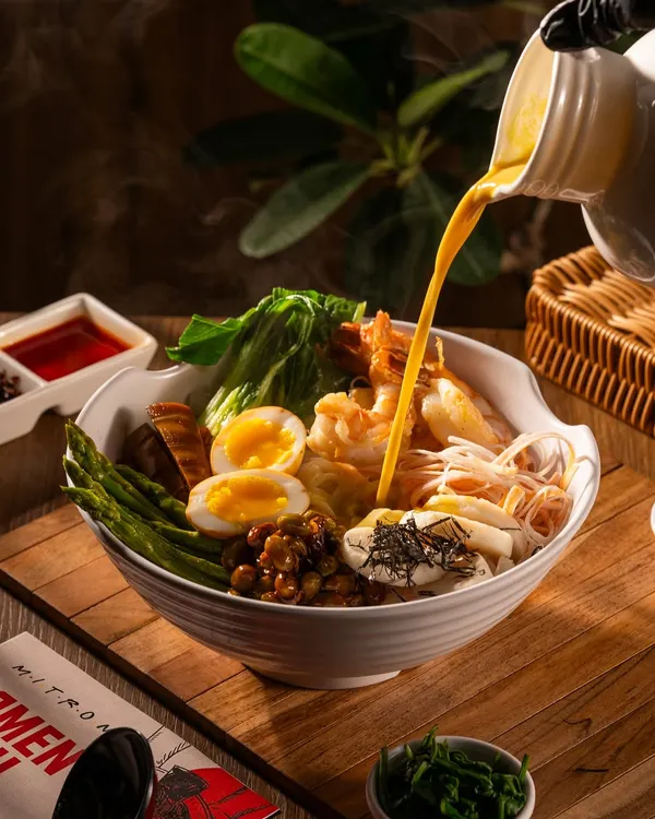 The moment a rich, steaming broth is poured over a bowl of ramen, bringing all the ingredients together.