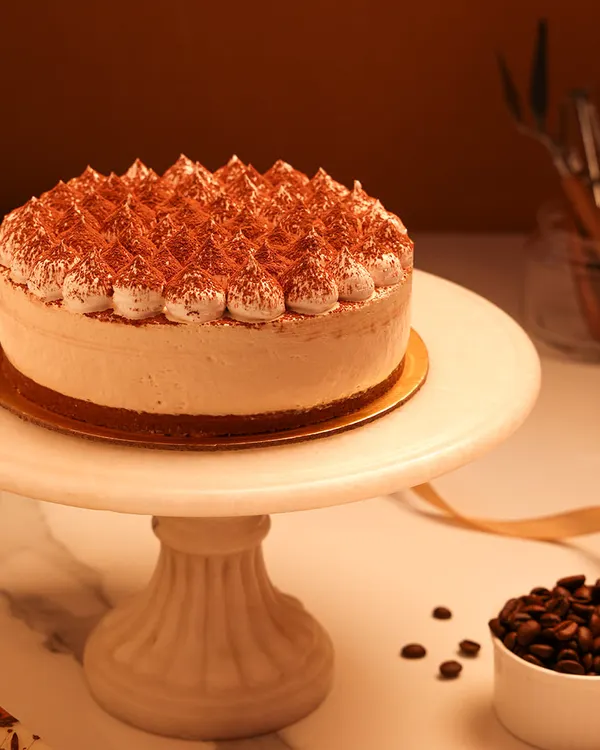 We present a taste of Italy with our classic Tiramisu cake. Featuring layers of coffee-soaked ladyfingers and creamy mascarpone, this cake is finished with piped cream and a generous dusting of cocoa powder for an authentic and elegant dessert experience.