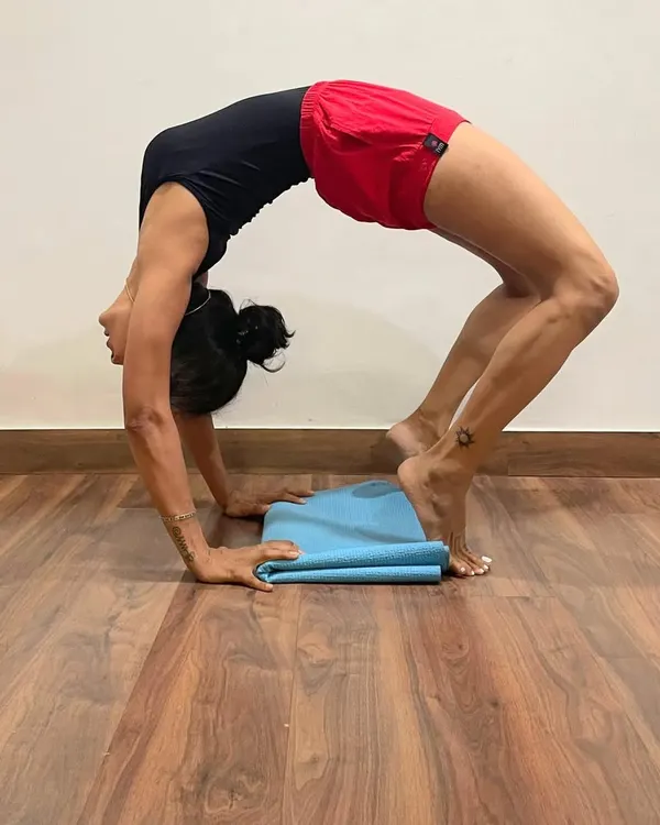 Urdhva Dhanurasana, or Wheel Pose, is a deep backbend that opens the entire front body. Here, the pose is performed with heels lifted on a folded mat to increase the arch in the upper back and open the shoulders.