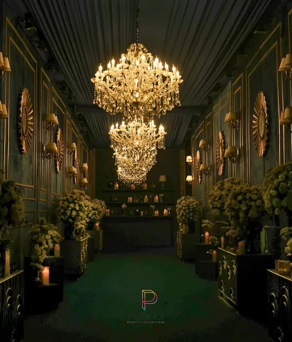 We designed this grand entrance to feel like stepping into another world. A dramatic hallway lined with towering floral arrangements, antique wall sconces, and a procession of crystal chandeliers creates an unforgettable first impression that is pure main character energy.