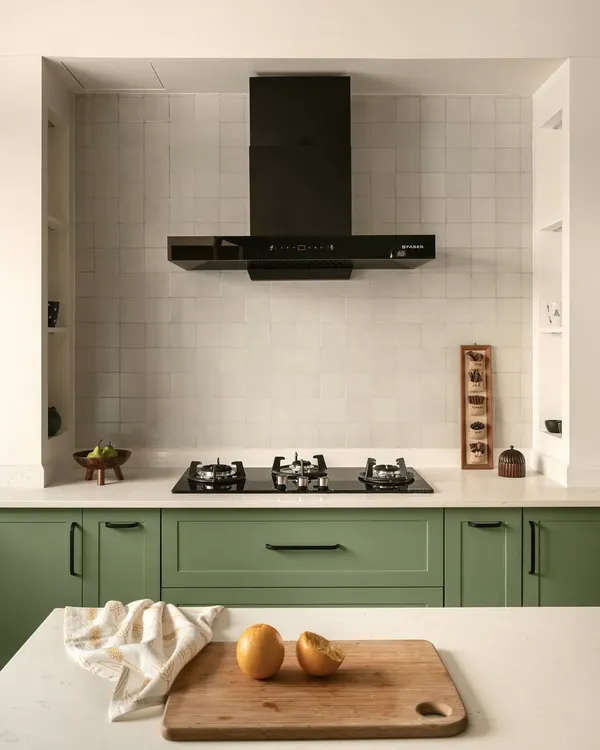 The gorgeous kitchen in the Earthy Hacienda home features sage green cabinets and a hooded cooktop with built-in niches for spices. The design is elevated by thoughtful details that enhance both aesthetics and functionality.