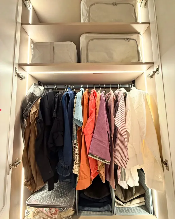 A well-lit wardrobe where clothes are hung neatly above, and seasonal items are stored in matching bags on the top shelf. This is a great example of using vertical space effectively.
