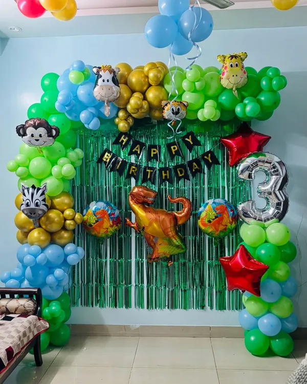 A fun jungle-themed birthday arch for a 3-year-old. This decoration features green, blue, and gold balloons, a green tinsel backdrop, and lots of animal foil balloons like a monkey, zebra, and dinosaur.
