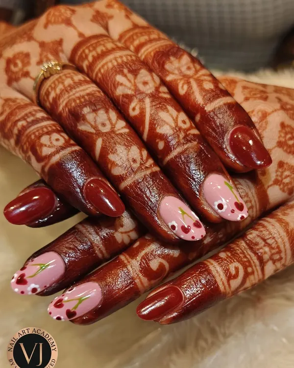 This beautiful bridal manicure combines rich maroon nails with delicate, hand-painted cherry blossom art on a soft pink base. The design perfectly complements the intricate mehndi, creating a look that balances tradition with modern elegance.
