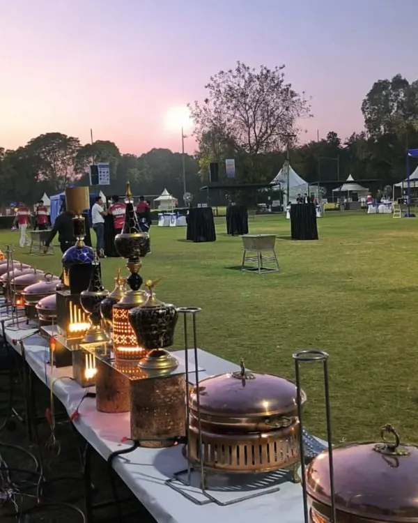 An outdoor buffet line set against a beautiful sunset. Our team arranges everything to perfection, using decorative lanterns and traditional copper serveware to create a magical dining experience on the open lawn.