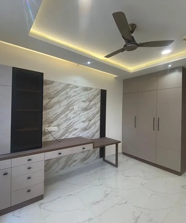 This bedroom combines a built-in wardrobe with an integrated study desk against a marble-textured wall panel. The design is both space-efficient and stylish.