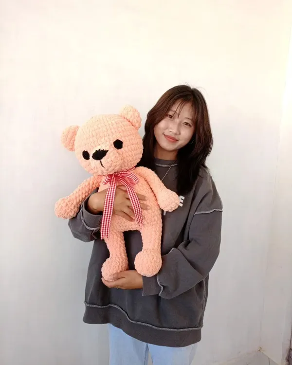 Here I am with a large, soft-pink teddy bear I just finished. These big plushies are made with extra-chunky yarn and are perfect for hugging.