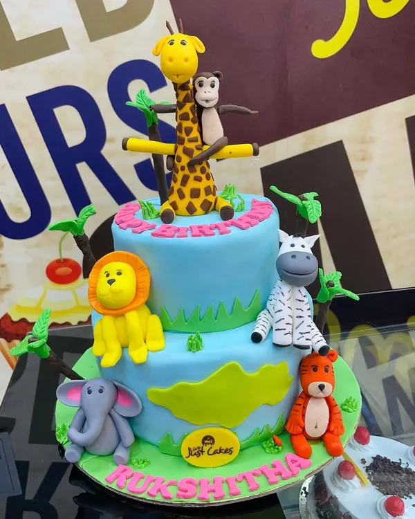 An exciting 3.5kg two-tiered jungle theme cake featuring a whole crew of hand-sculpted fondant animals, including a giraffe, lion, zebra, and monkey.