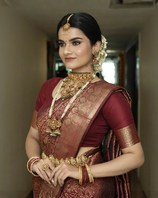 A side profile showcasing the complete South Indian bridal look, from the traditional maang tikka and gajra in her hair to the layered temple necklaces. The makeup remains flawless and radiant from every angle.