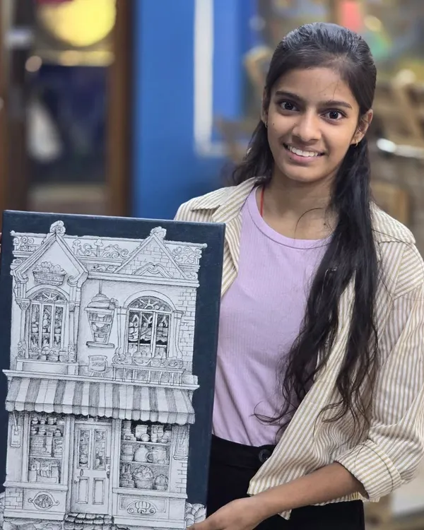 A proud student holds her completed micron pen drawing, an incredibly detailed illustration of a storefront that showcases her patience and precision with ink.