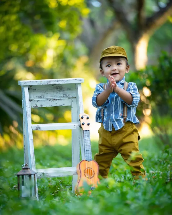 A happy little boy clapping his hands during his outdoor photoshoot. The lush green grass and soft background light create a beautiful, natural portrait.