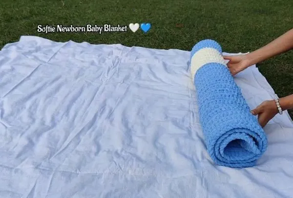 Rolling up a freshly made softie newborn baby blanket in a beautiful blue and white design. This shows the generous size and plush texture of the blanket.